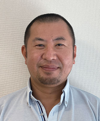 Portrait photo of a man in a light blue shirt standing in front of a light background.