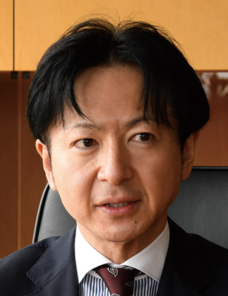 A professional headshot of a man in a suit, seated and looking slightly to the side, against an office background. Ideal for corporate or case study use.