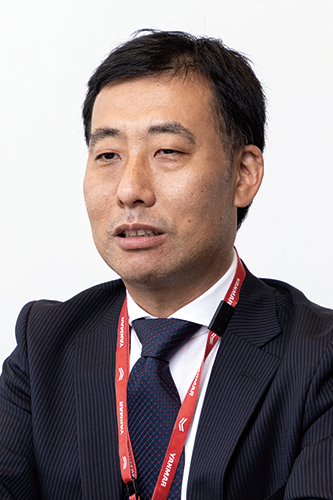 Portrait of a Yanmar executive wearing a suit, tie, and red lanyard, facing forward against a plain background.