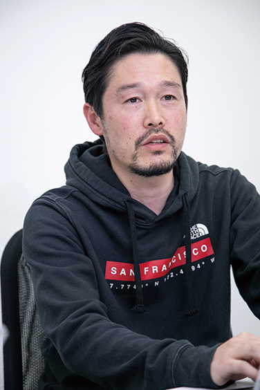 A portrait of a person with short dark hair and a trimmed beard, wearing a black hoodie with 'San Francisco' text, sitting and looking slightly to the side. The background is plain and light-colored.