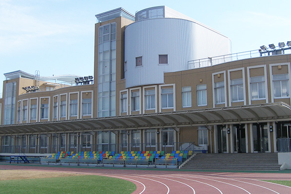 The exterior view of Satoe Gakuen school building, featuring modern architecture, large windows, and a covered seating area beside a running track.