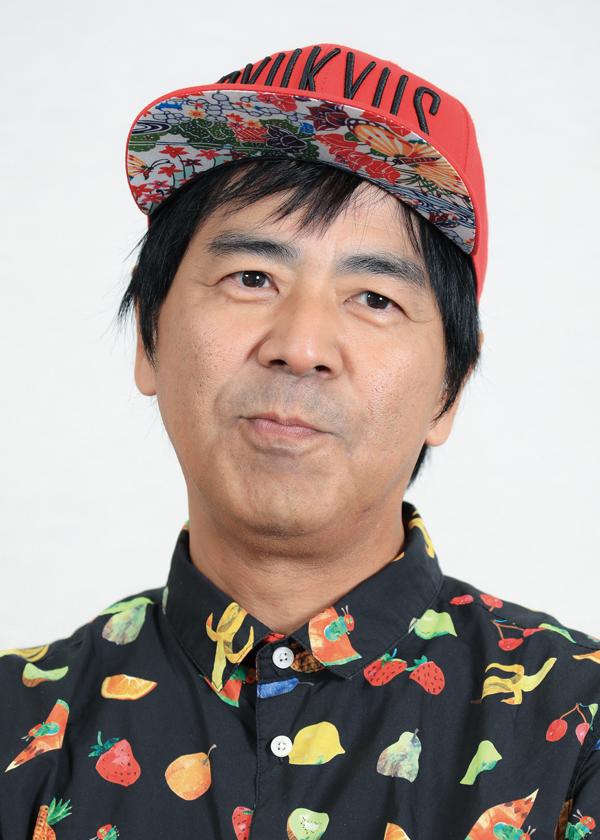 A portrait photo of a person wearing a colorful fruit-patterned shirt and a red cap with multicolored patterns on the underside of the brim, on a light background.