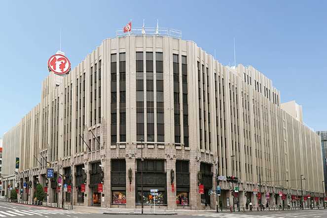 Exterior view of the Mitsukoshi Isetan Department Store in Tokyo, featuring the building's architecture and street corner location under a clear blue sky.