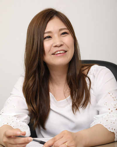 A woman in a white blouse is smiling while sitting at a desk.
