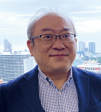 Portrait of an executive from Itochu Corporation with a cityscape background, wearing glasses and a blue blazer.