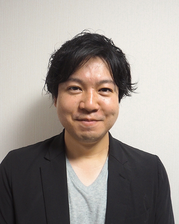 Portrait photo of a speaker for the SoftBank case study, featuring an individual in a black jacket and gray shirt, standing in front of a light-colored wall.