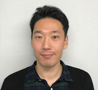 Portrait of a man with short dark hair, wearing a dark sweater over a checker-patterned shirt, used for a case study in Japan.