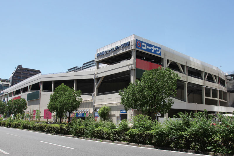 Exterior view of the Kohnan Shoji store building in Japan, showcasing its modern multi-level architecture surrounded by trees on a sunny day.