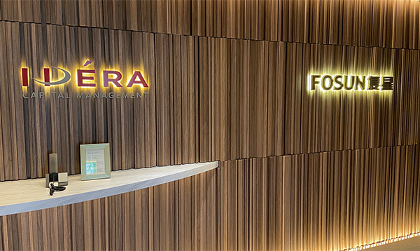 Office signage for IDERA Capital Management and FOSUN displayed on a wood-paneled wall with soft lighting.