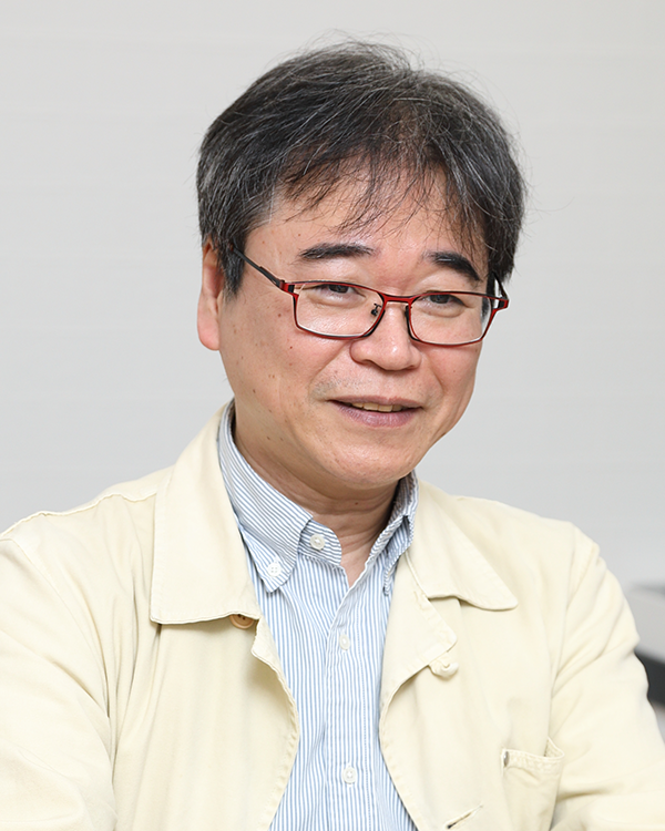 A middle-aged man wearing glasses and a light-colored jacket, indoors, looking slightly to the side.