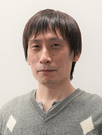 Portrait of an East Asian man with short dark hair wearing a grey sweater, facing the camera with a neutral expression, against a plain background.
