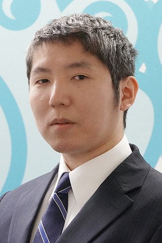 Portrait of a businessman in a suit and tie with a blue patterned background.