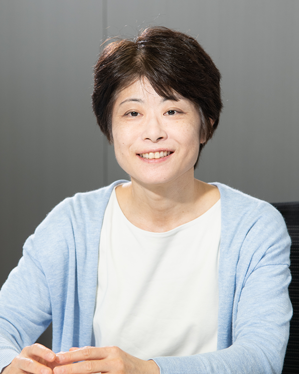 Portrait of a person from the Toshiba case study, seated and smiling, wearing a light blue cardigan and white shirt.