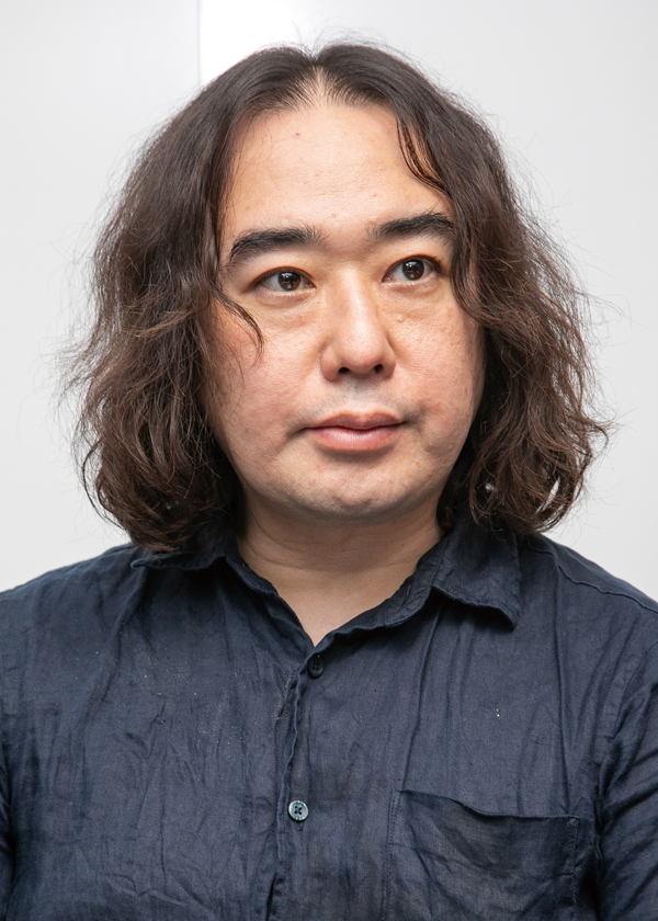 A portrait photograph of a man with medium-length dark hair wearing a dark shirt, set against a plain background. (Moneytree Umegaya)