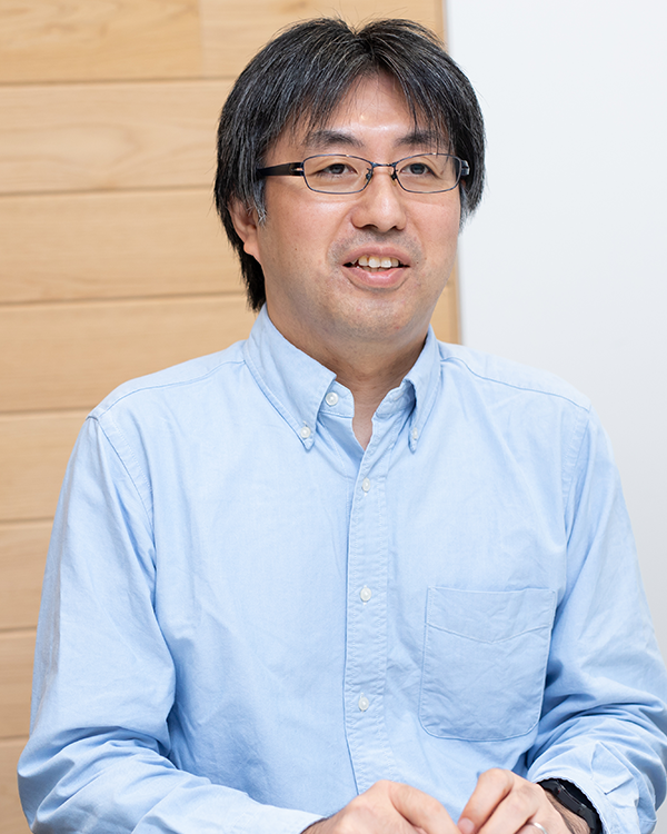 A portrait of a speaker in the Applibot case study, showing a person in a light blue shirt and glasses, seated indoors against a wooden and white background.