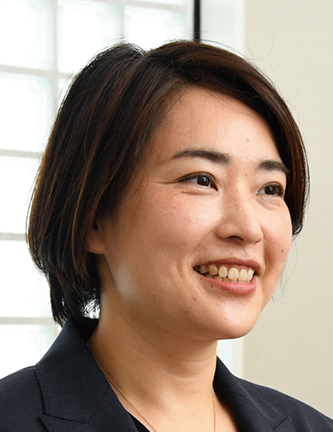 A professional portrait of a smiling woman with short dark hair, wearing a dark blazer, photographed indoors.