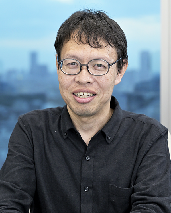 Portrait of a person wearing glasses and a black shirt, seated in front of a window with a cityscape background, used for the DMM case study.