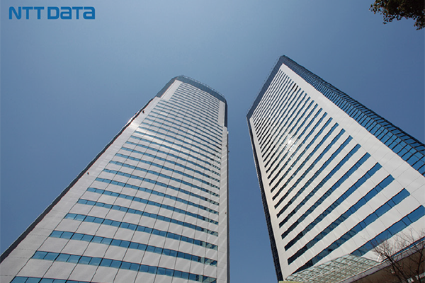 Two tall, modern skyscrapers with reflective windows under a clear blue sky, featuring the NTT DATA logo in the top left corner.