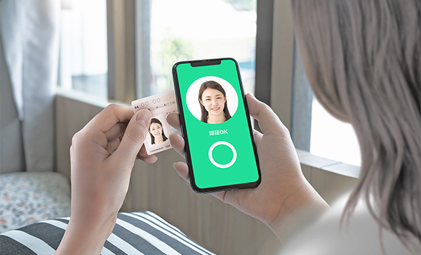 A person using a mobile phone for ID verification, holding an identification card and matching their facial image with the app on the phone screen.