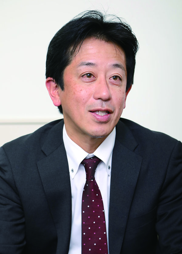 A person wearing a dark suit, white shirt, and maroon polka-dot tie.