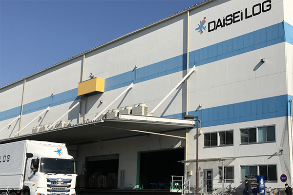 The exterior of a Daisei Logistics warehouse featuring a Daisei-branded truck parked near the loading dock on a clear day.