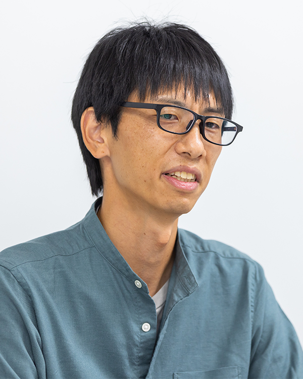 A man with short black hair wearing glasses and a blue shirt, looking at the camera in a portrait-style photograph.