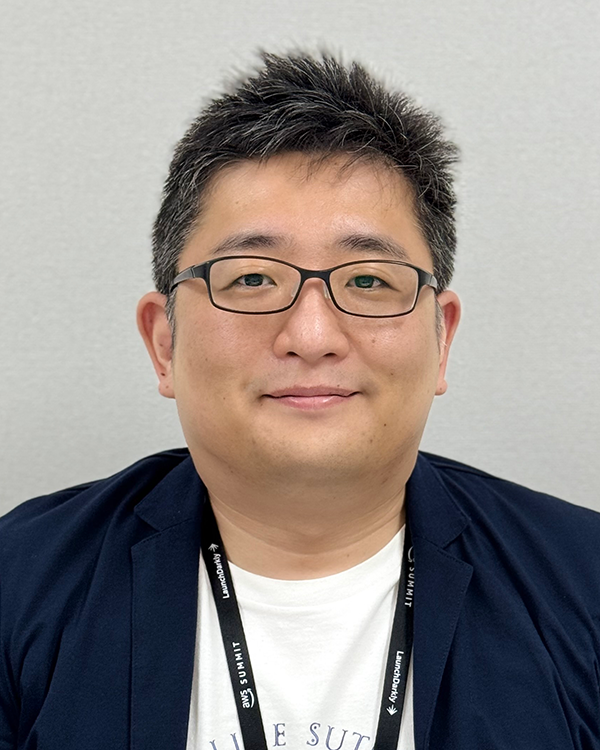 Portrait photo of a speaker for the Felissimo case study, featuring an individual wearing glasses and a dark jacket, with a neutral gray background.