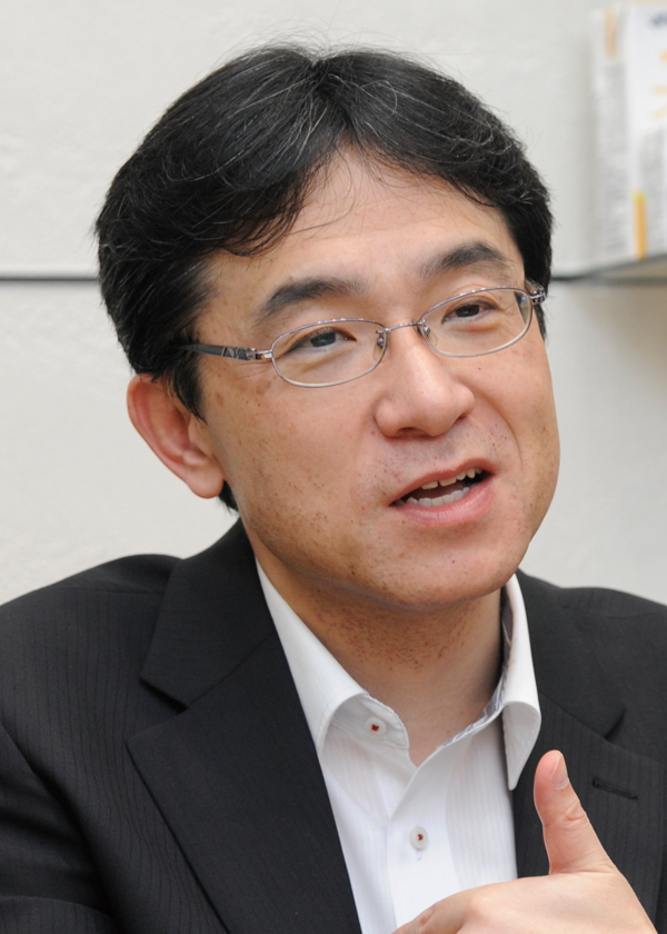A person wearing a black suit and white collared shirt, with a blurred face, giving a thumbs-up gesture.