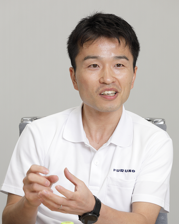 Portrait of a speaker from the Furuno case study, showing a person in a white Furuno polo shirt, seated and gesturing while speaking.