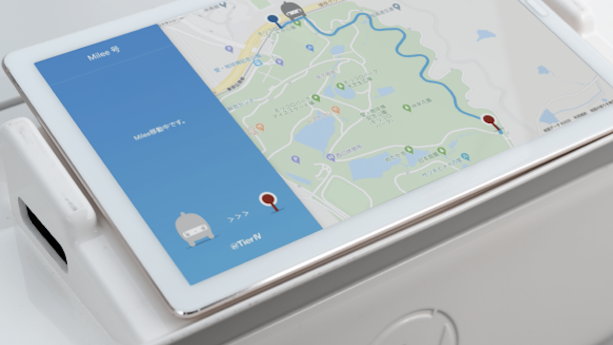 A close-up of a tablet showing a Tier IV map interface with navigation features, Milee branding, and location markers in Japanese, on a white mounting stand.