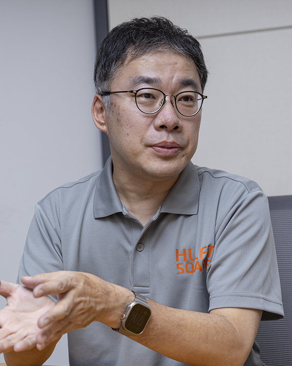 A man wearing glasses and a gray polo shirt sits and gestures with his hands during an interview, featured in the Saison Technology case study.