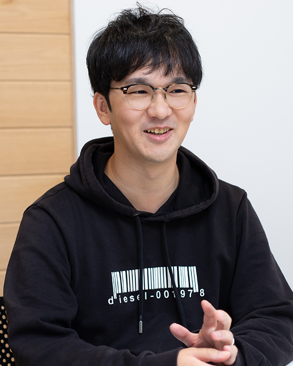 A man wearing glasses and a black hoodie with a barcode design, sitting and speaking in an indoor setting. This image is used for the Applibot case study speaker profile.
