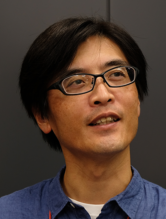 Portrait of a man wearing glasses and a blue shirt, facing slightly upward with a neutral background.