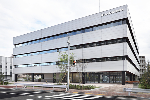 The exterior view of the Furuno headquarters building, showcasing a modern multi-story office structure with large windows and a sleek facade.