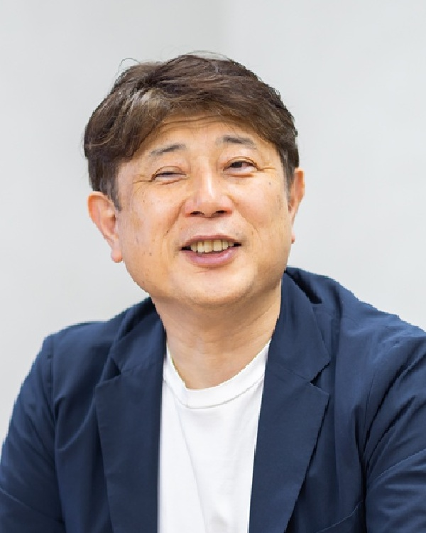 Portrait of Mr. Katori from Yasashii Te, featured in the AWS Solution Case Study. The image shows a man in a light blazer and white shirt, smiling and looking slightly off camera, with a neutral background.