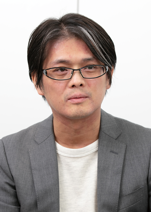 Portrait of a man with short dark hair, wearing glasses and a gray business suit over a white shirt, against a plain background.