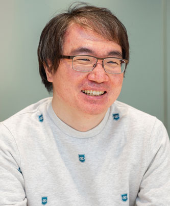 Portrait of a person wearing glasses and a light-colored shirt, smiling, photographed for a V-Cube solution case study.