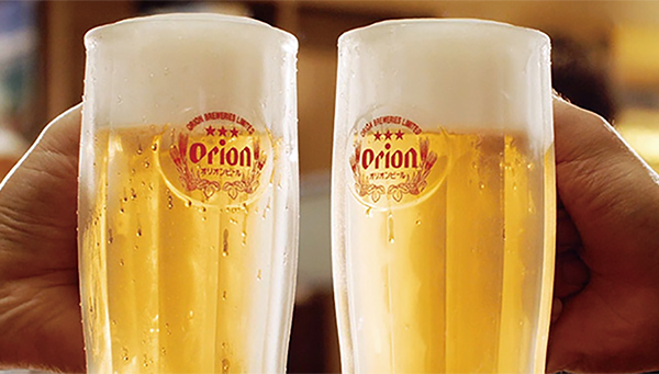 Two hands holding and toasting with Orion beer glasses filled with golden beer and foam on top.