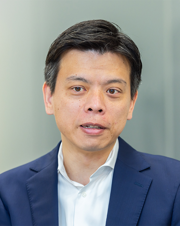 A professional business portrait photo of a person in a suit, facing forward with a neutral background. Image size is 600x750 pixels.