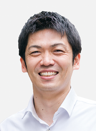 A portrait of a smiling man with short dark hair, wearing a white shirt, facing the camera against a light background.