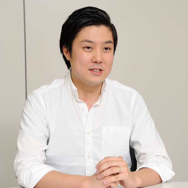A person in a white shirt seated at a table, speaking during an interview. Neutral background.
