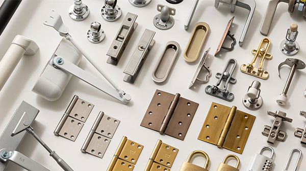A top-down view of an assortment of Japanese hardware products, including door hinges, locks, latches, handles, and other metal hardware components, displayed on a white background.