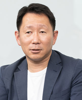Portrait photo of a male speaker featured in the Fujitsu case study, wearing a dark blazer and white shirt, against a neutral background.