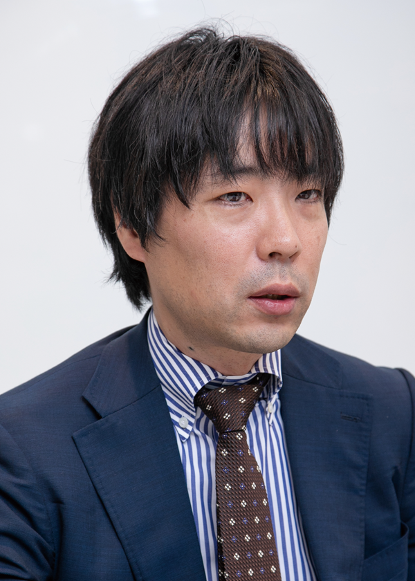 A person wearing a navy suit, a blue and white striped shirt, and a brown patterned tie.