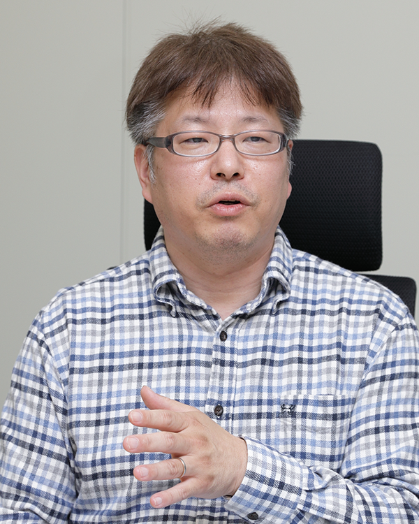 A man in glasses and a checkered shirt speaks while seated in an office chair, representative image from the MK System case study interview.