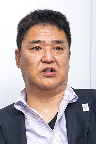 Portrait photo of a business professional wearing a suit and collared shirt, speaking in an indoor setting.