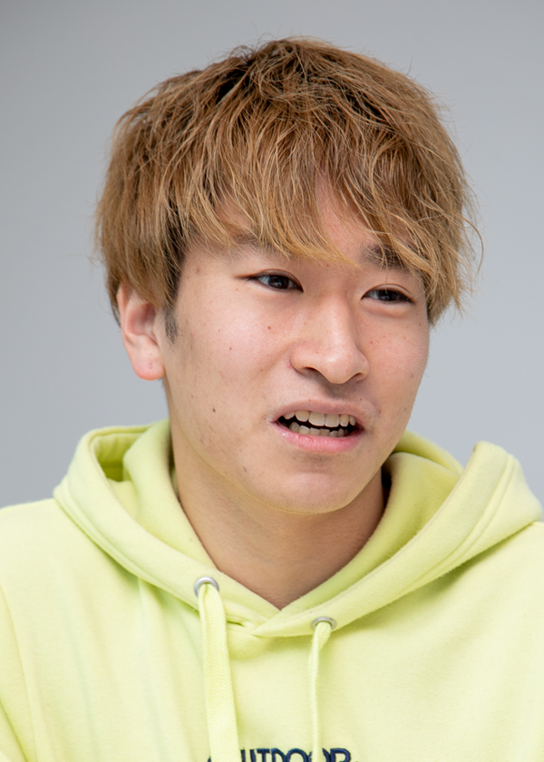 A person wearing a yellow hoodie is interviewed, likely for a TV Tokyo case study. The image shows a close-up of the individual's face against a plain background.