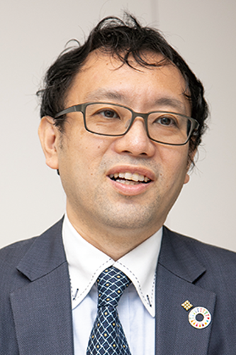 Business portrait of Mr. Niino from Itoki, wearing glasses, a suit, and a tie, with an SDGs badge on his lapel.