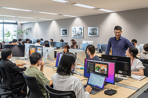 A modern office environment with multiple employees collaborating and working at desktop computers. The atmosphere is productive, with people engaging in teamwork and discussion around their workstations.