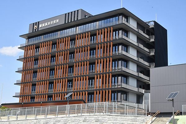 Exterior view of Rikuzen Takata City Hall, a modern multi-story building with vertical wooden accents and a glass facade in Rikuzen Takata, Japan.